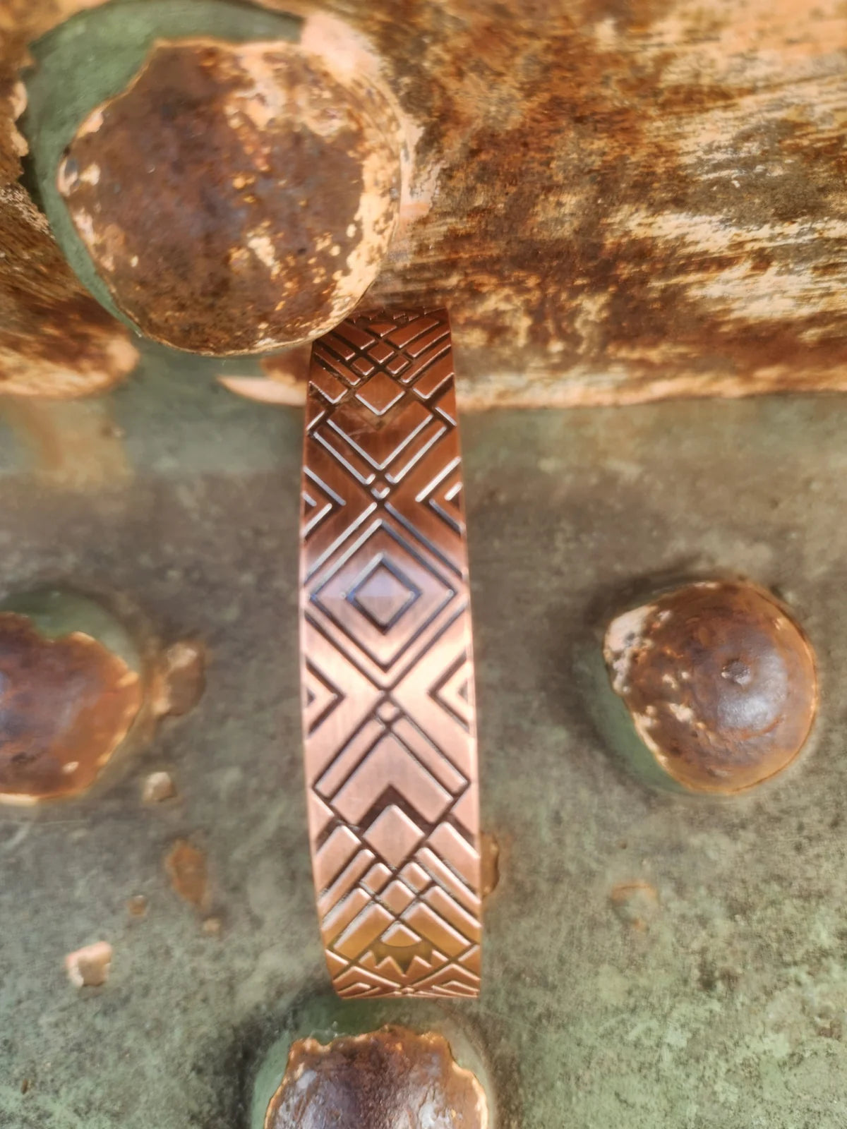 Detailed side-on view of diamond and cross geometric design on copper cuff