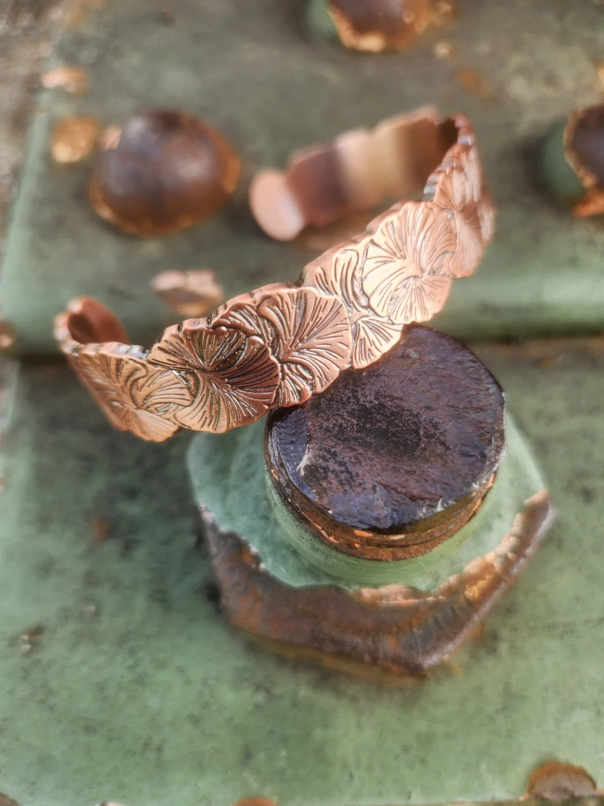 Angled view of floral copper cuff with overlapping flower motifs on weathered green metal