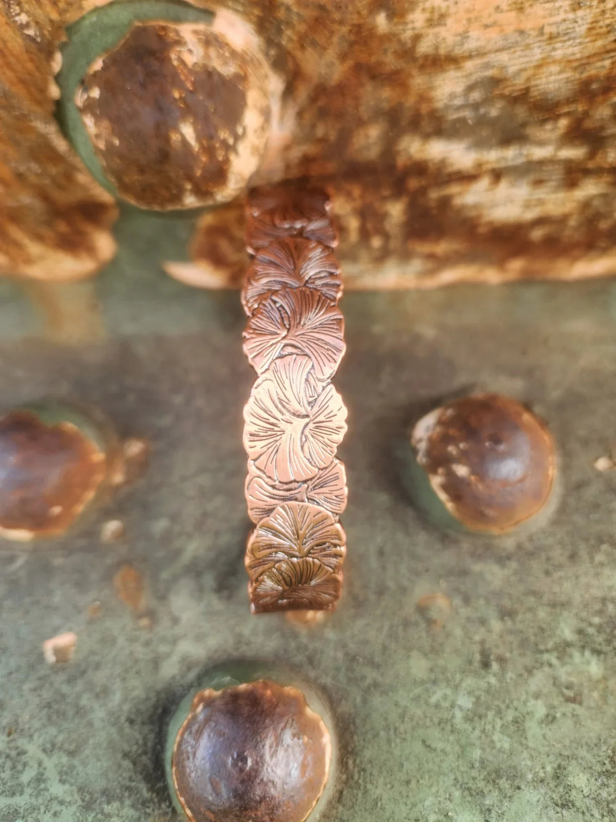 Vertical detail showing raised flower design on copper cuff bracelet