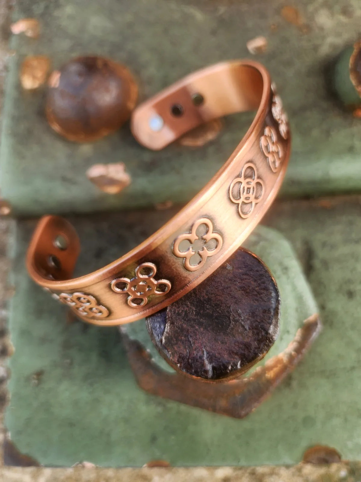 Angled close-up of four-leaf magnetic copper cuff resting on weathered green metal