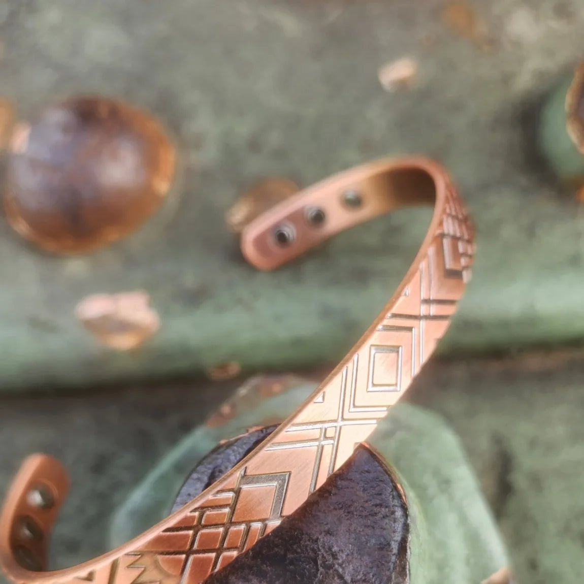 Angled view of slim geometric copper cuff against weathered green metal