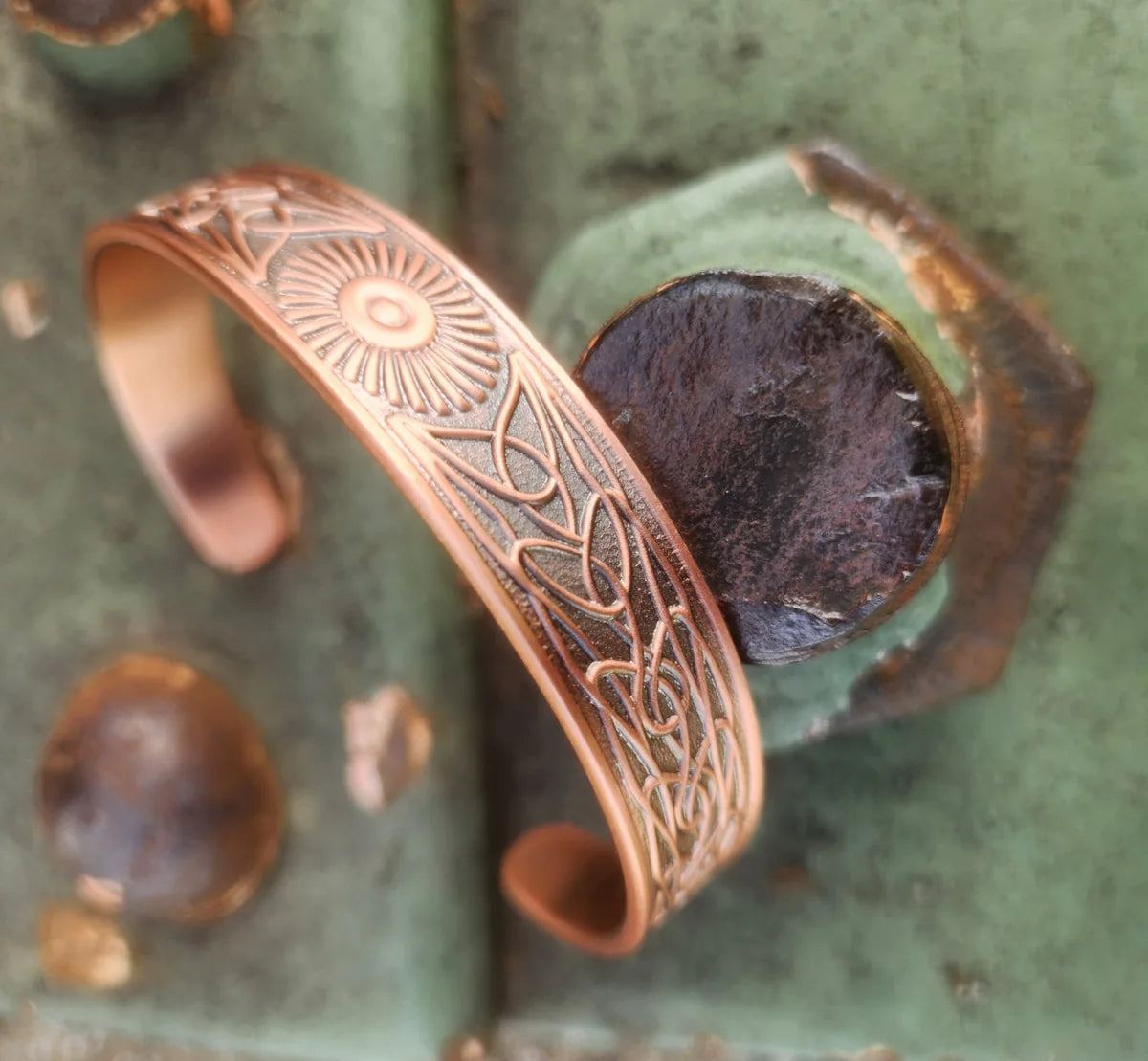Angled view of sunburst and knot copper cuff on weathered green metal