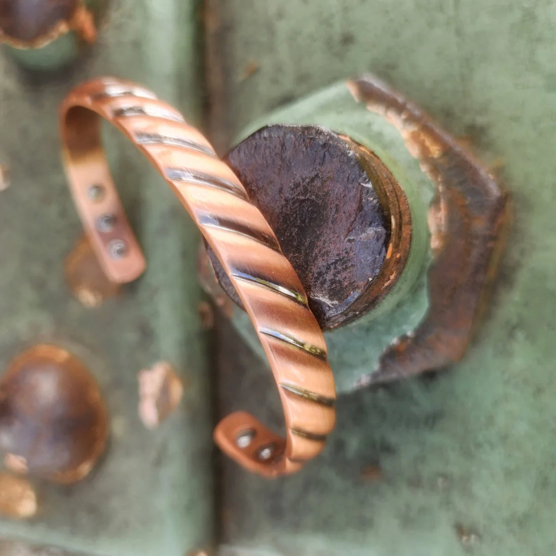 Angled view of twisted rope magnetic copper cuff on rustic green metal